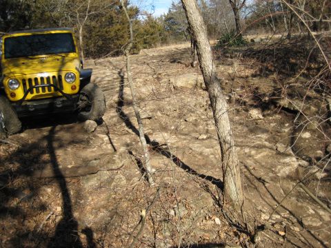 2005 Jeep Wrangler - A yellow 2005 Jeep Wrangler tackles a challenging off-road course with steep inclines and rocky obstacles.