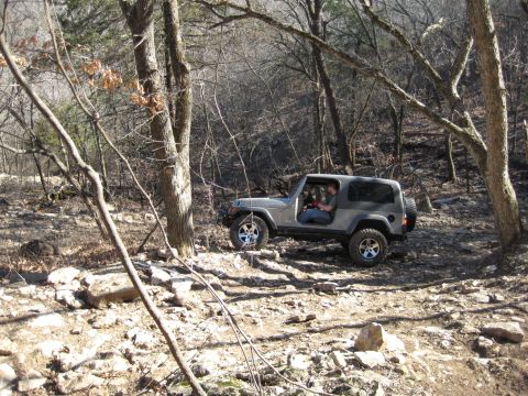 2005 Jeep Wrangler - A Jeep Wrangler navigates a challenging off-road path through a wooded area with rocky terrain.
