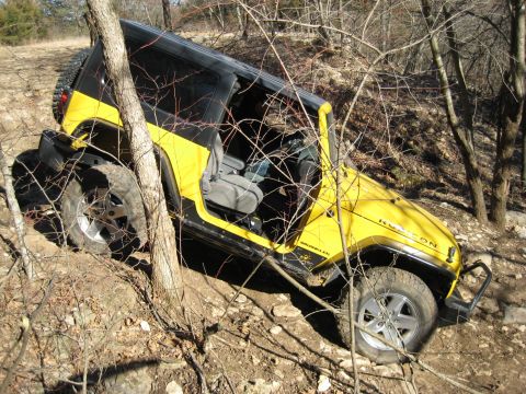 2005 Jeep Wrangler - A yellow Jeep Wrangler Rubicon navigates a challenging off-road course through trees and rocks.
