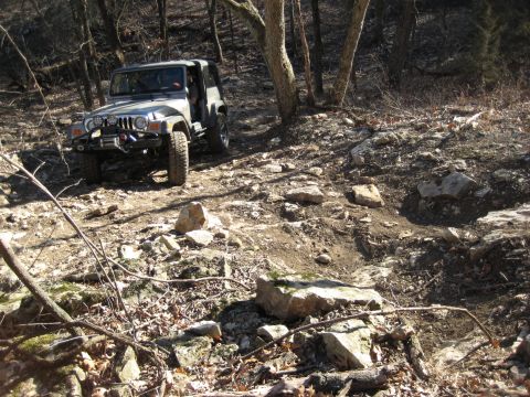 2005 Jeep Wrangler - A gray 2005 Jeep Wrangler navigates a challenging rocky and wooded off-road path.