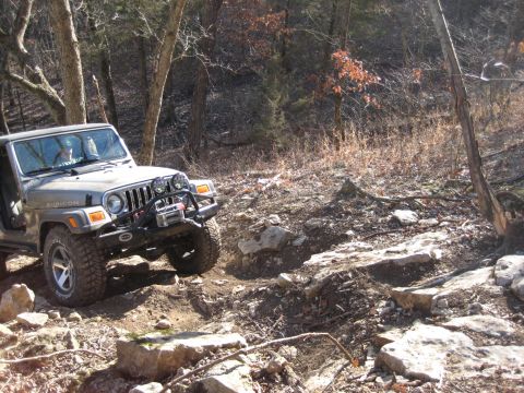 2005 Jeep Wrangler - A Jeep Wrangler navigates a rocky, wooded trail, demonstrating its off-road capabilities.