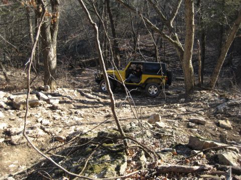 2005 Jeep Wrangler - A yellow Jeep Wrangler navigates a rocky path through a wooded area.