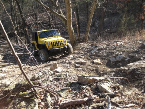 2005 Jeep Wrangler - A yellow Jeep Wrangler navigates a challenging, rocky path through a wooded area during the day.