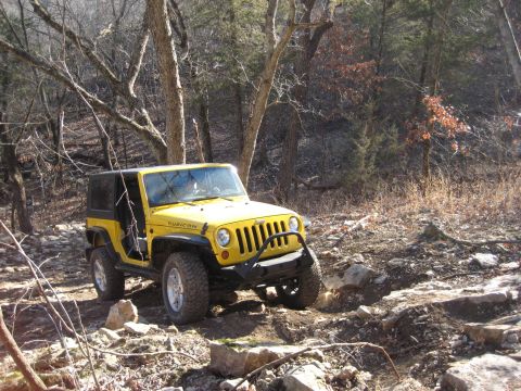2005 Jeep Wrangler - A yellow Jeep Wrangler navigates a challenging rocky terrain in a wooded area.
