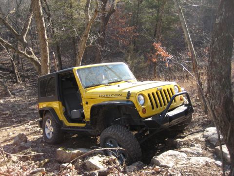 2005 Jeep Wrangler - A yellow 2005 Jeep Wrangler Rubicon is shown off-roading through a rocky, wooded area.
