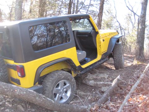 2005 Jeep Wrangler - A yellow 2005 Jeep Wrangler Rubicon navigates a rocky trail, its door open to the wooded surroundings.