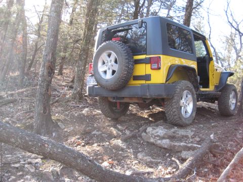 2005 Jeep Wrangler - Yellow Jeep Wrangler navigating a rocky off-road trail in a wooded area.