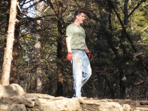 2005 Jeep Wrangler - A man stands in a wooded area, wearing work gloves and jeans stained with dirt.