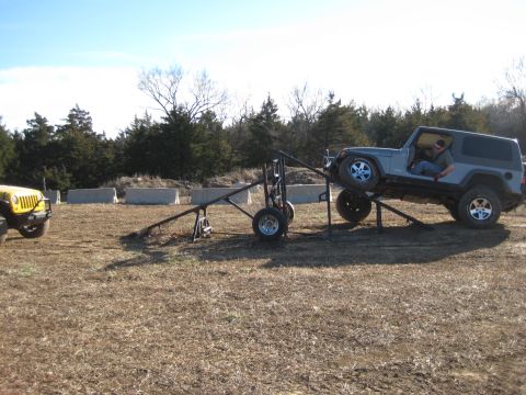 2005 Jeep Wrangler - A gray Jeep Wrangler is positioned on a metal ramp structure, with a yellow Jeep visible to the left. The scene appears to be an outdoor ob…