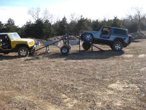 2005 Jeep Wrangler - Two Jeep Wranglers are positioned in an outdoor area, with one vehicle elevated on a metal ramp structure.