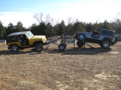 2005 Jeep Wrangler - Two Jeep Wranglers are positioned on an off-road obstacle course, one yellow and one gray, connected by a trailer structure.