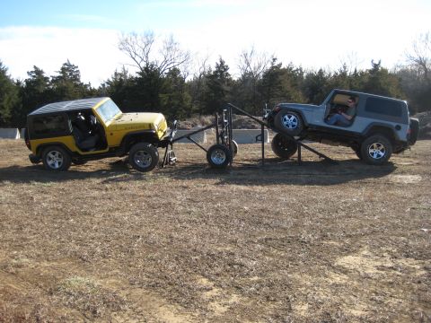 2005 Jeep Wrangler - Two Jeep Wranglers are positioned on an off-road course, one yellow and one gray, connected by a trailer apparatus.