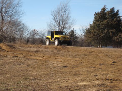 2005 Jeep Wrangler - A yellow Jeep Wrangler sits on a dirt mound under a clear blue sky.