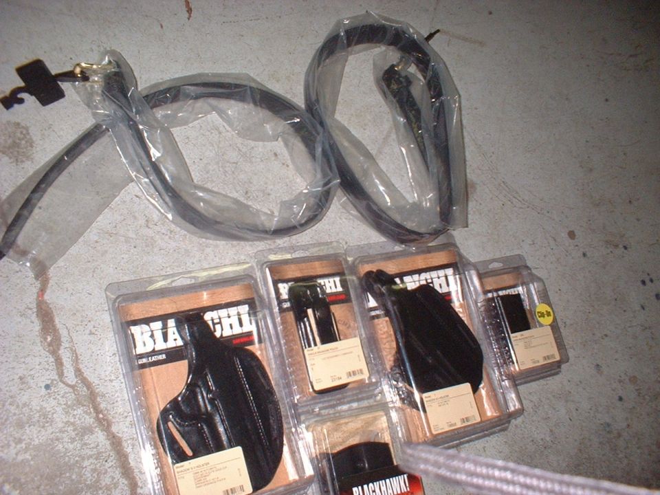 Several Blackhawk! gun holsters in plastic packaging and two black belts in plastic packaging on a concrete floor