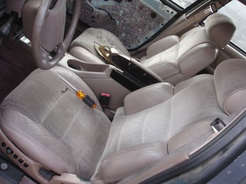 1993 Ford Taurus - The interior of a car shows worn seats and a disassembled dashboard area, with a screwdriver resting on the driver's seat.