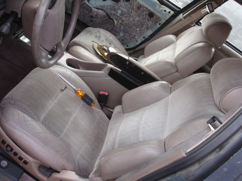 Car interior with beige seats, steering wheel, and center console. Screwdriver on driver's seat