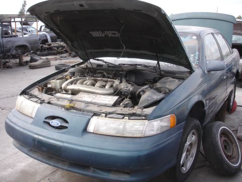 1993 Ford Taurus - This teal Ford Taurus SHO is in a junkyard with its hood open, revealing the engine and the SHO emblem.