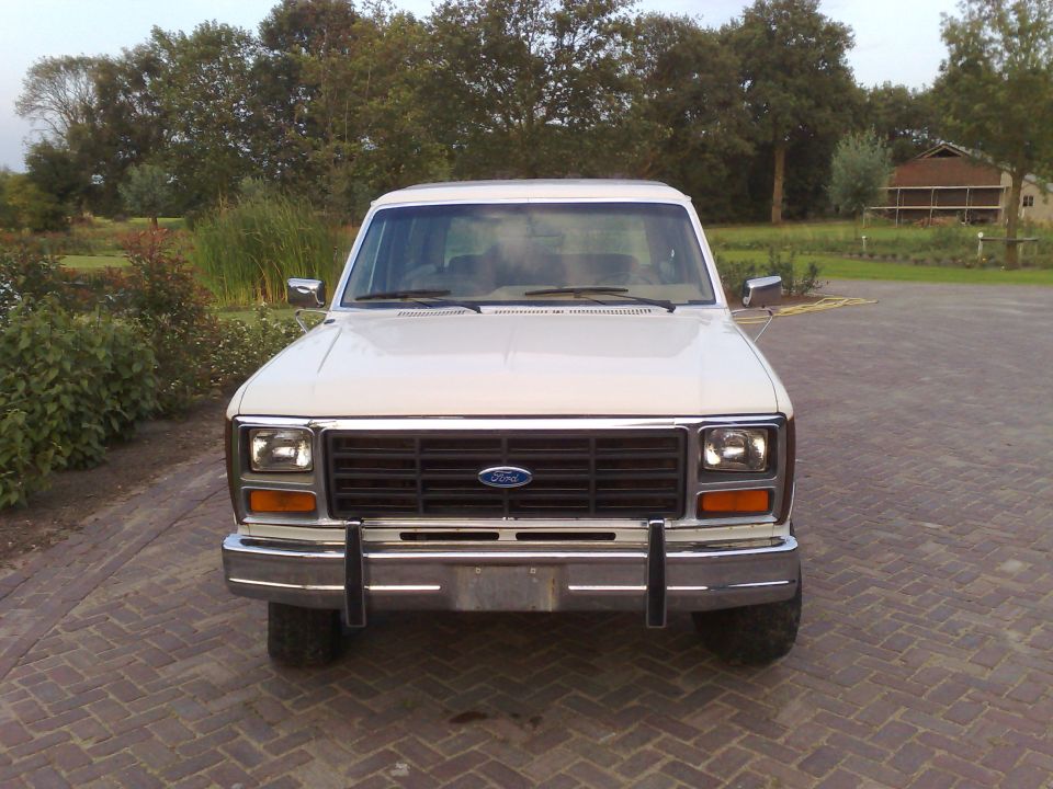 Front view of a white 1980s Ford Bronco parked on a brick driveway