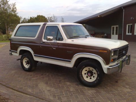 1984 Ford Bronco - This two-tone Ford Bronco is parked outside a building with a covered overhang.