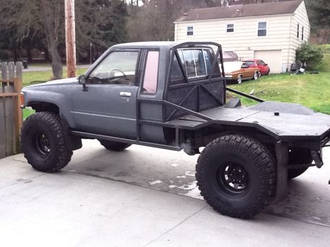 1988 Suzuki Samurai - This modified flatbed pickup truck features a custom roll cage and off-road tires, suggesting a 1989 model year.