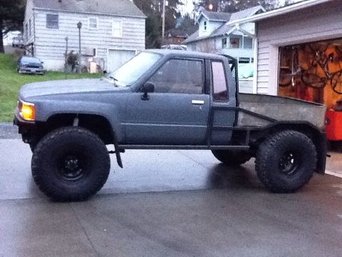 1988 Suzuki Samurai - This modified Toyota pickup truck features oversized tires and a custom flatbed, seen from the side.