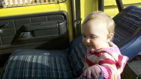 1978 Ford Bronco - A baby sits in the passenger seat of a vintage yellow Ford Bronco, with the door panel and seat fabric visible.