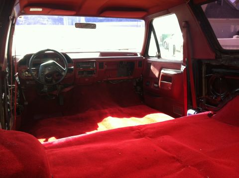 1991 Ford Bronco - The interior of a 1991 Ford Bronco shows red carpeting and a red dashboard with the steering wheel.