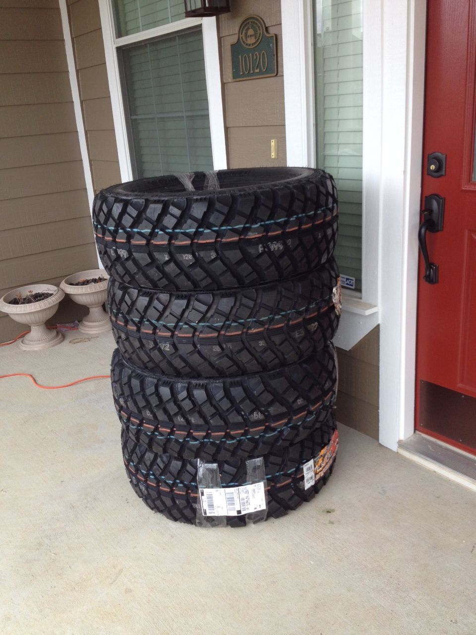 Stack of four new off-road tires on a concrete porch, bound with plastic wrap