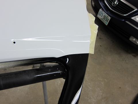 1987 Dodge 1500 - Close-up of a white car door edge being worked on, with a dark vehicle visible in the background.