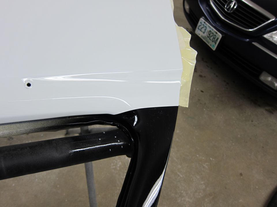White car door edge with black trim, masking tape, and a dark car in the background