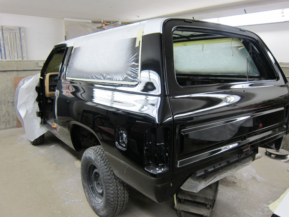 Black Dodge Ramcharger SUV, rear quarter view, being worked on in a garage. Windows are taped off