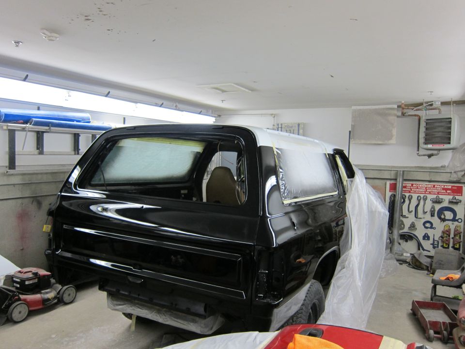 Black SUV with white roof, covered in plastic and tape, in a garage with a lawnmower nearby