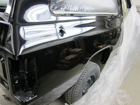 1987 Dodge 1500 - The rear section of a black pickup truck is visible, undergoing repairs and covered in protective plastic.