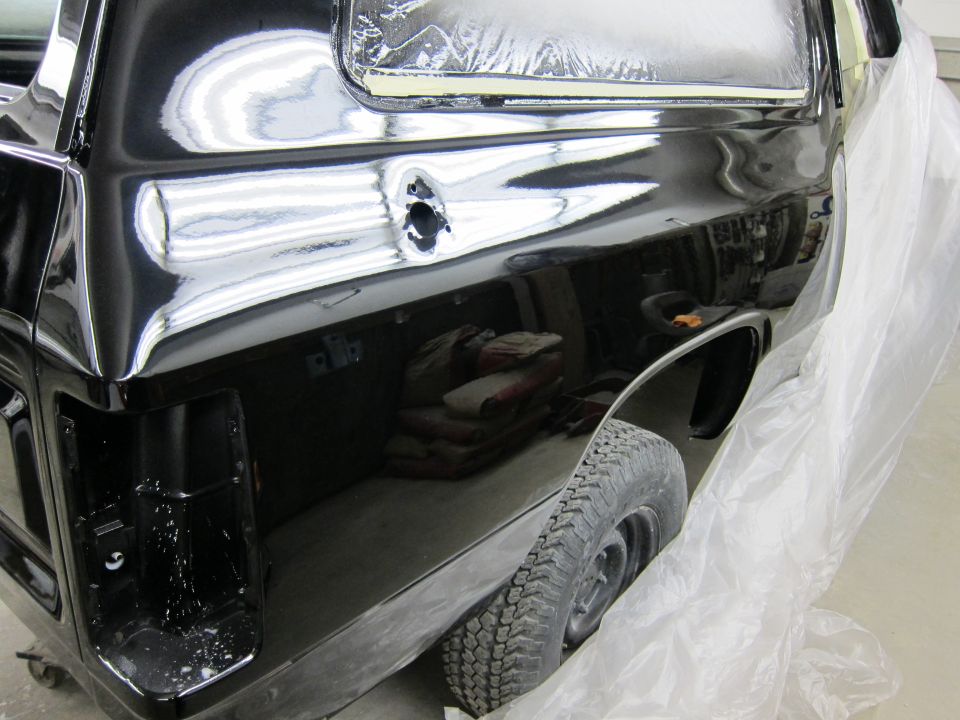 Black pickup truck rear quarter panel, covered in plastic sheeting, with visible bodywork and a tire