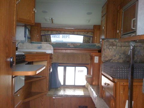 1968 Ford Mustang - The interior of a truck camper shows a sleeping area above a window and a kitchen setup.