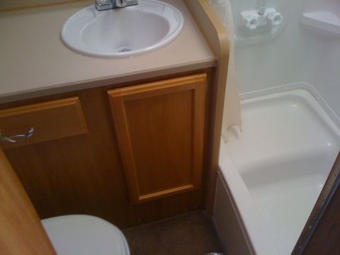 1968 Ford Mustang - The interior of an RV bathroom shows a sink, toilet, and a shower stall with white fixtures.