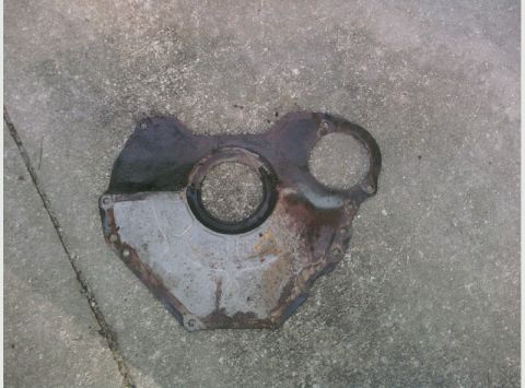 1995 Ford Bronco - This is a metal engine timing cover with two circular openings, lying on a concrete surface.