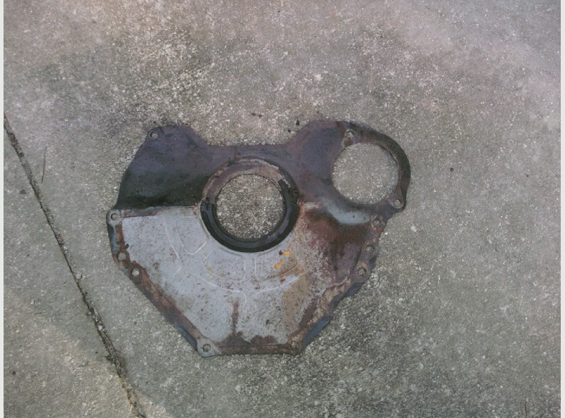 Rusty removed cast engine timing cover with central seal bore lying on concrete
