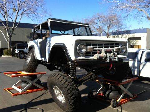 1968 Ford Bronco - A modified 1968 Ford Bronco is elevated on hydraulic jacks, revealing its lifted suspension and large tires.