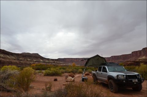 1990 Chevrolet Suburban - Pickup truck with rooftop tent camping in a desert canyon under a cloudy sky.
