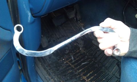 1990 Ford Bronco - A person holds a uniquely shaped wrench inside a vehicle's cabin, near the pedals.