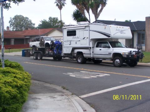 1968 Ford Mustang - A white truck camper is parked on the street, towing a trailer carrying another white pickup truck.