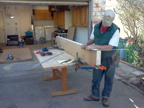 1996 Ford Bronco - A man measures and marks a piece of wood in a garage setting with tools and a workbench.
