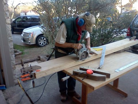 1996 Ford Bronco - A man works on a wooden plank with a circular saw, with a silver Cadillac and a black SUV visible in the background.