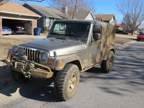 2005 Jeep Wrangler - A muddy silver Jeep Wrangler is parked on the side of a street in front of houses.