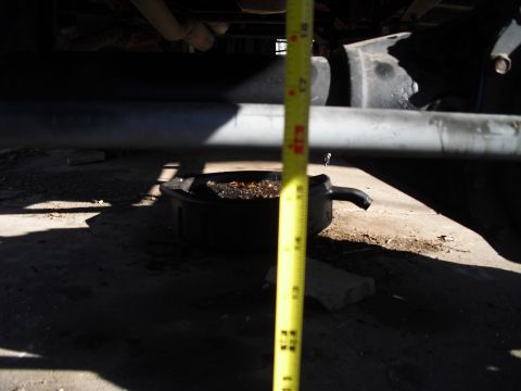 1986 Ford Bronco - A yellow tape measure is used to gauge the distance between the vehicle's frame and an oil collection pan.