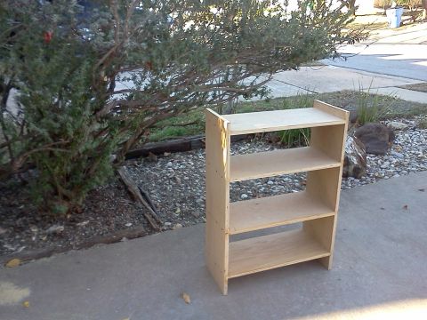 1996 Ford Bronco - A simple, unfinished wooden shelving unit sits outdoors on a paved surface.