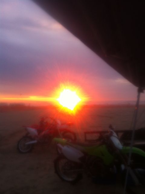 1989 Ford Bronco - Dirt bikes are parked on the sand as the sun sets over the ocean.