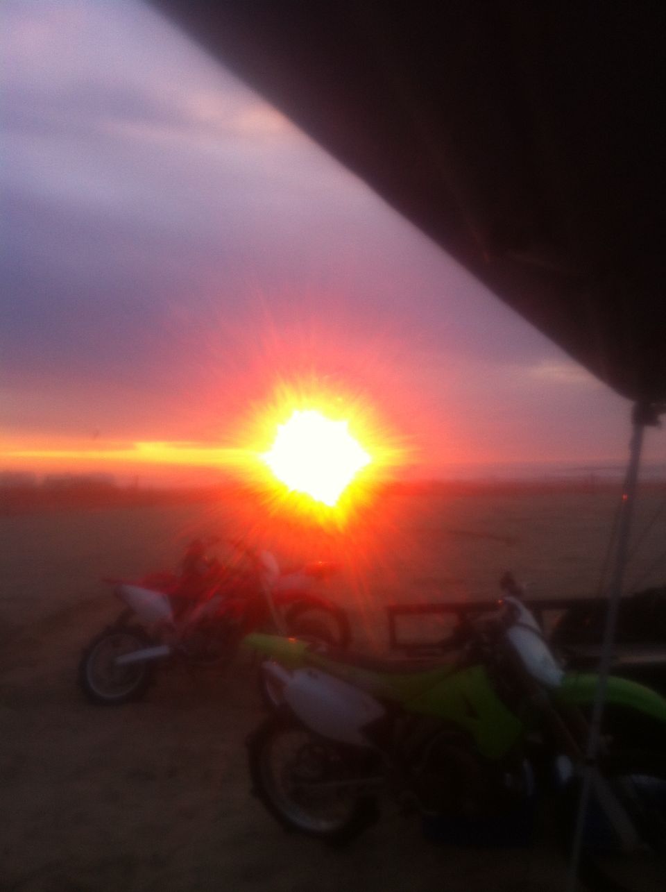 Two dirt bikes parked on a beach during a vibrant sunset