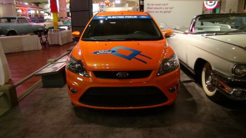 1993 Ford Taurus - An orange Ford Focus electric concept car is displayed at an auto show next to a white classic convertible.